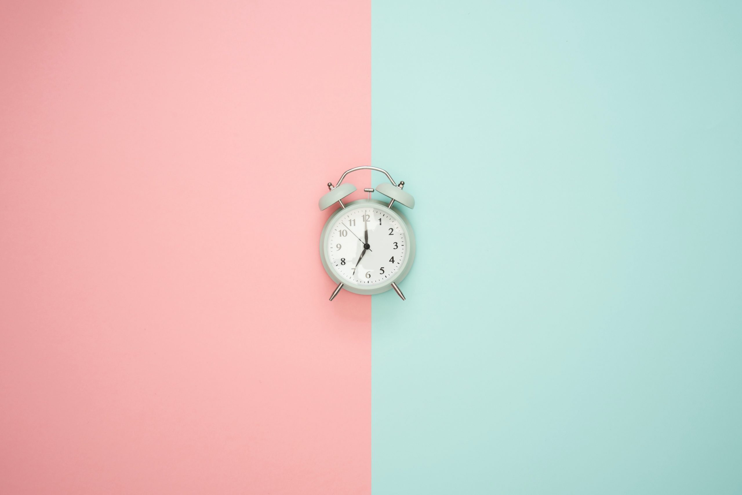A clock in front of a two tone background split in half between pink and green.